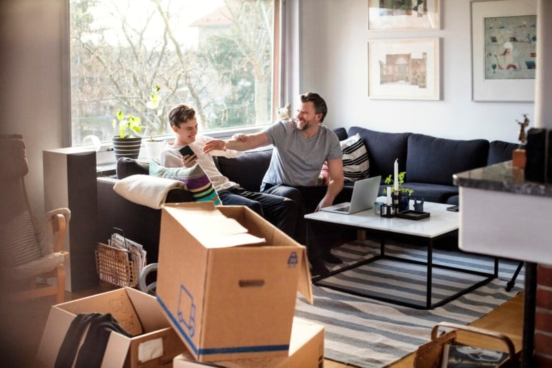 En mann og en ung gutt sitter i sofaen med pappesker på stuegulvet