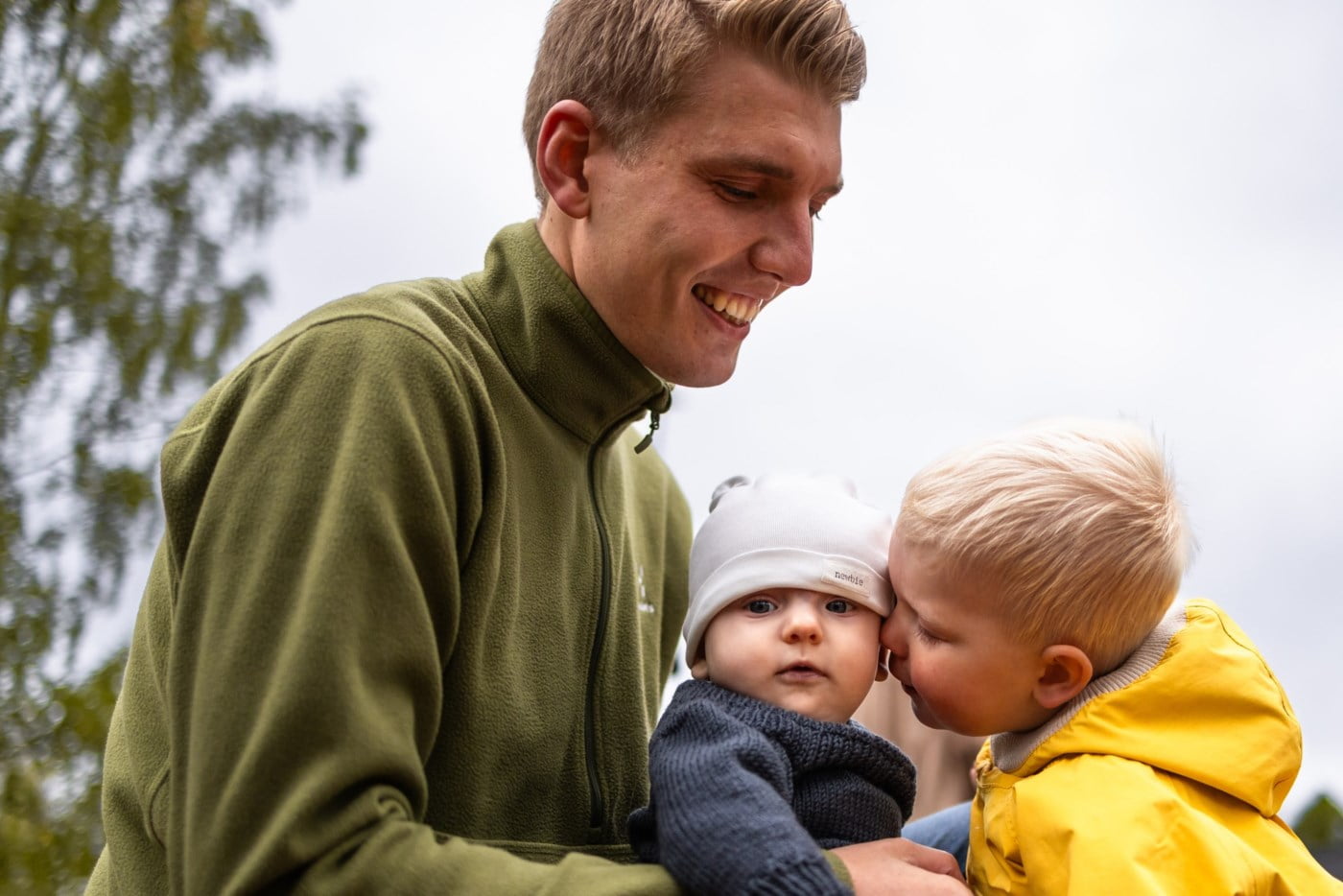 En mann holder en baby som får et nuss på kinnet av en liten gutt
