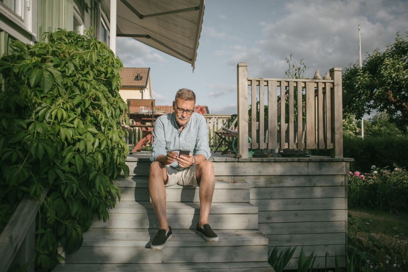 En mann sitter på verandaen med en mobil i hånden